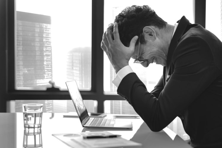 Man Sitting At His Desk Holding his Head In His Hands After Realizing That He Made A Huge Mistakes