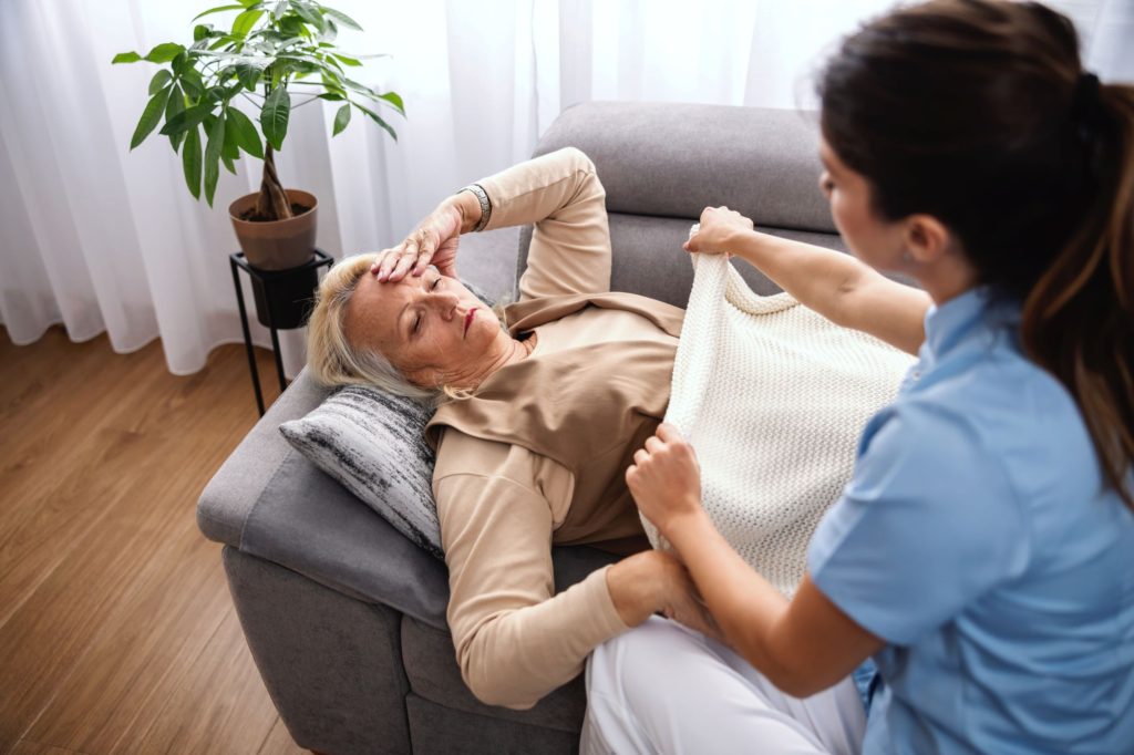 Woman Lying Down On A Sofa With A Nurse Taking Care Of Her